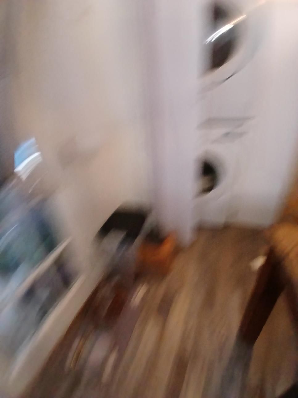 Blurred view of a laundry room with a stacked washer and dryer unit, wooden floor, and cabinet.