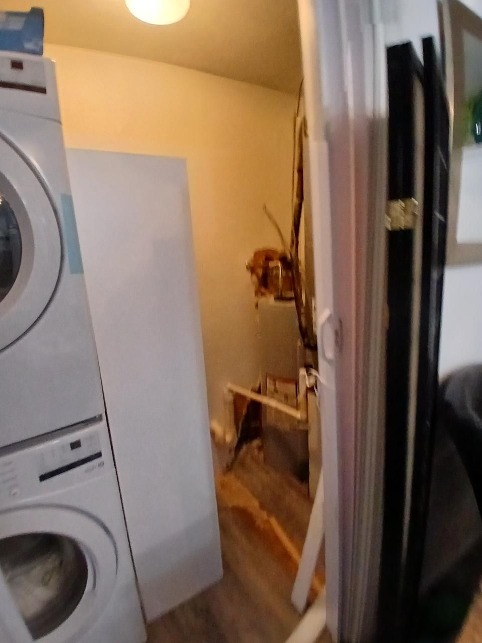 Laundry room with stacked white washer/dryer, white door, and exposed wall damage.