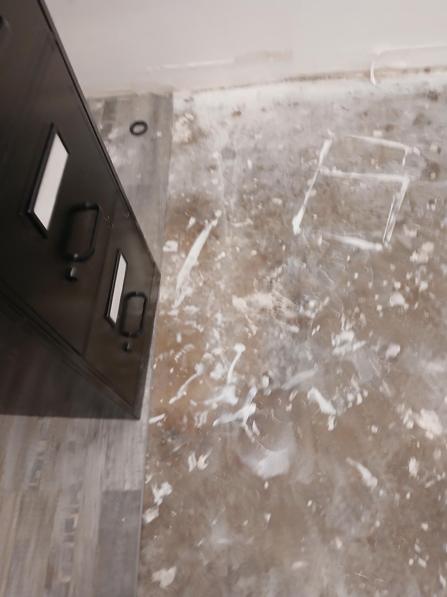 A black shield leans against a wall, splattered paint on the floor.