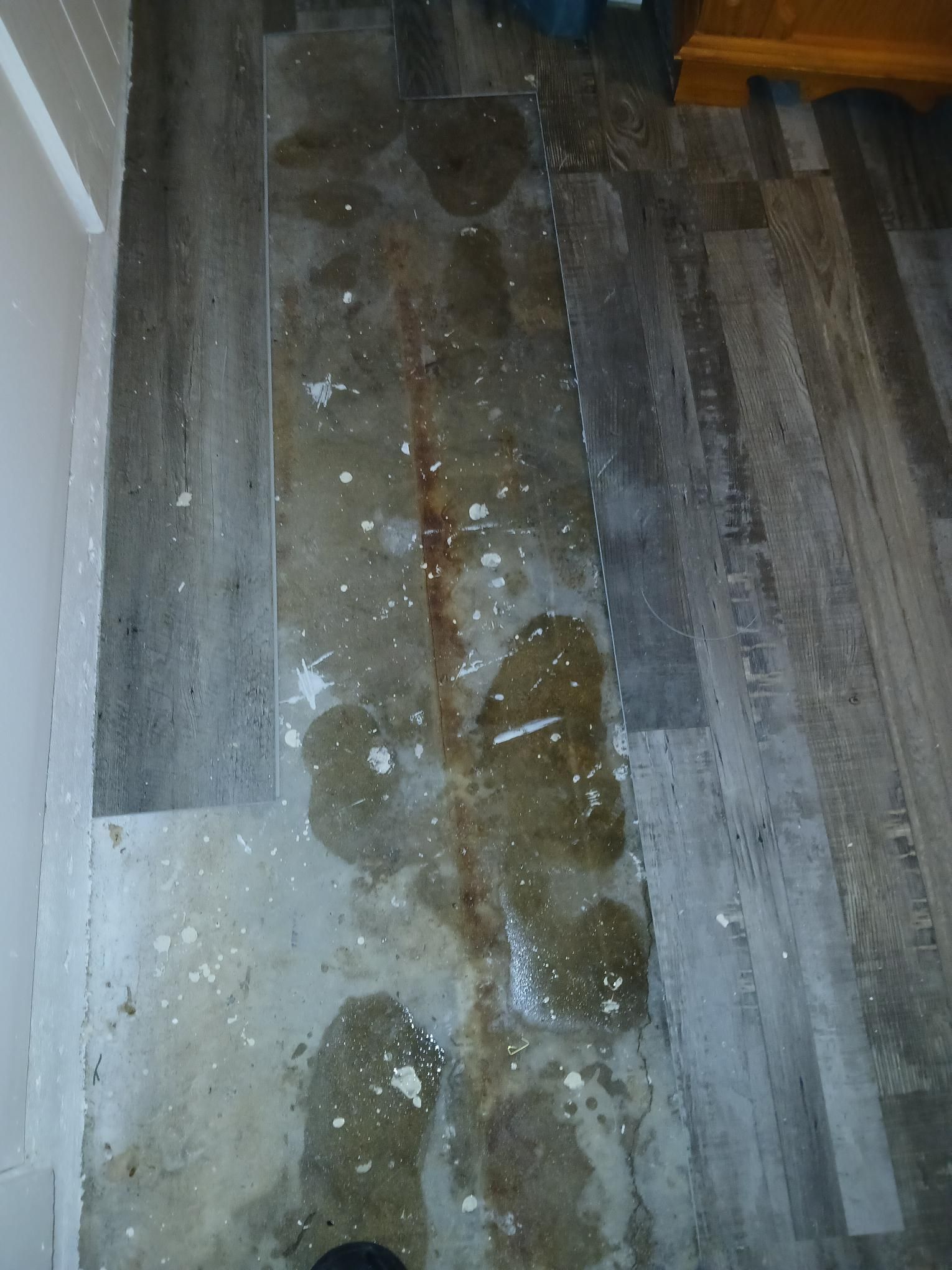 Wet, damaged vinyl plank flooring with water stains and white residue.