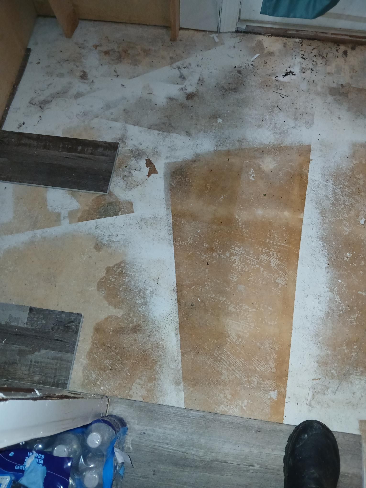 Floor with patches of different materials, including wood and beige. White residue scattered across the surface.