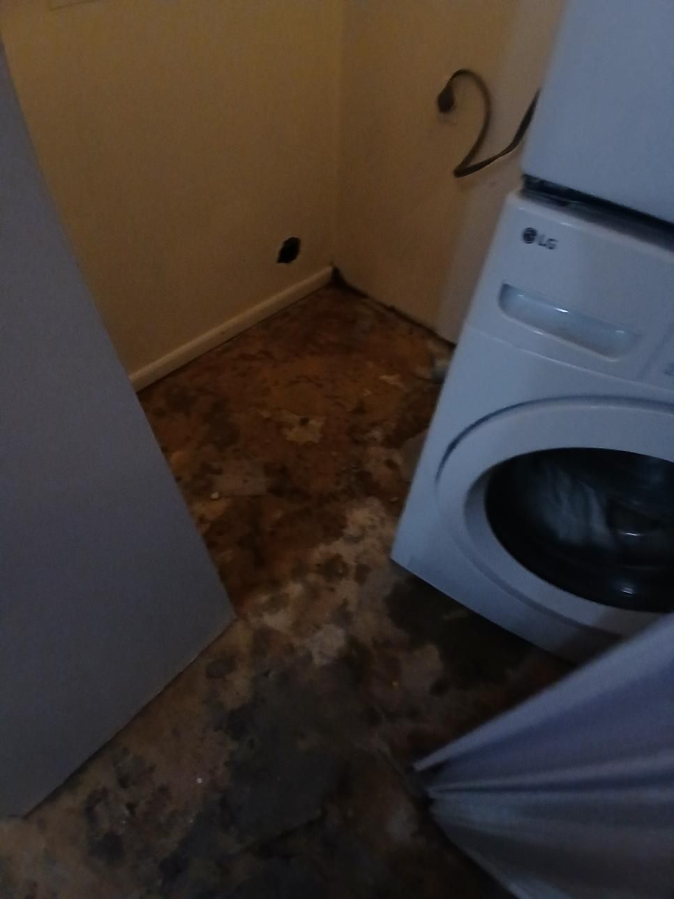 Laundry room with washing machine, stained floor, and electrical outlet.