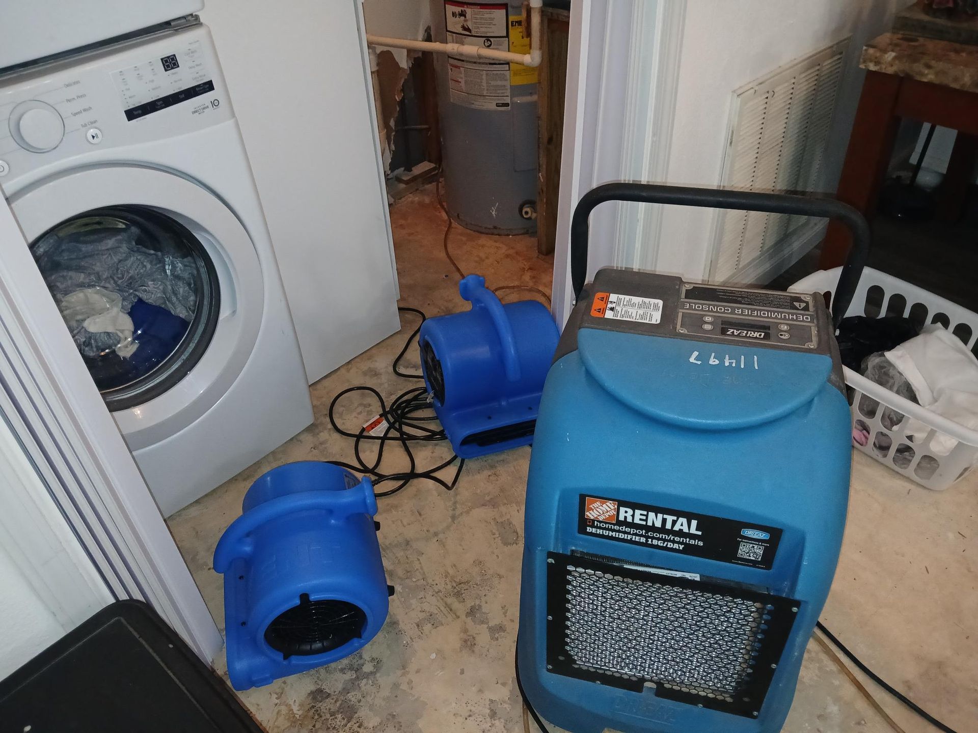 Basement with washing machine, dehumidifier, and two blue fans; flood cleanup in progress.