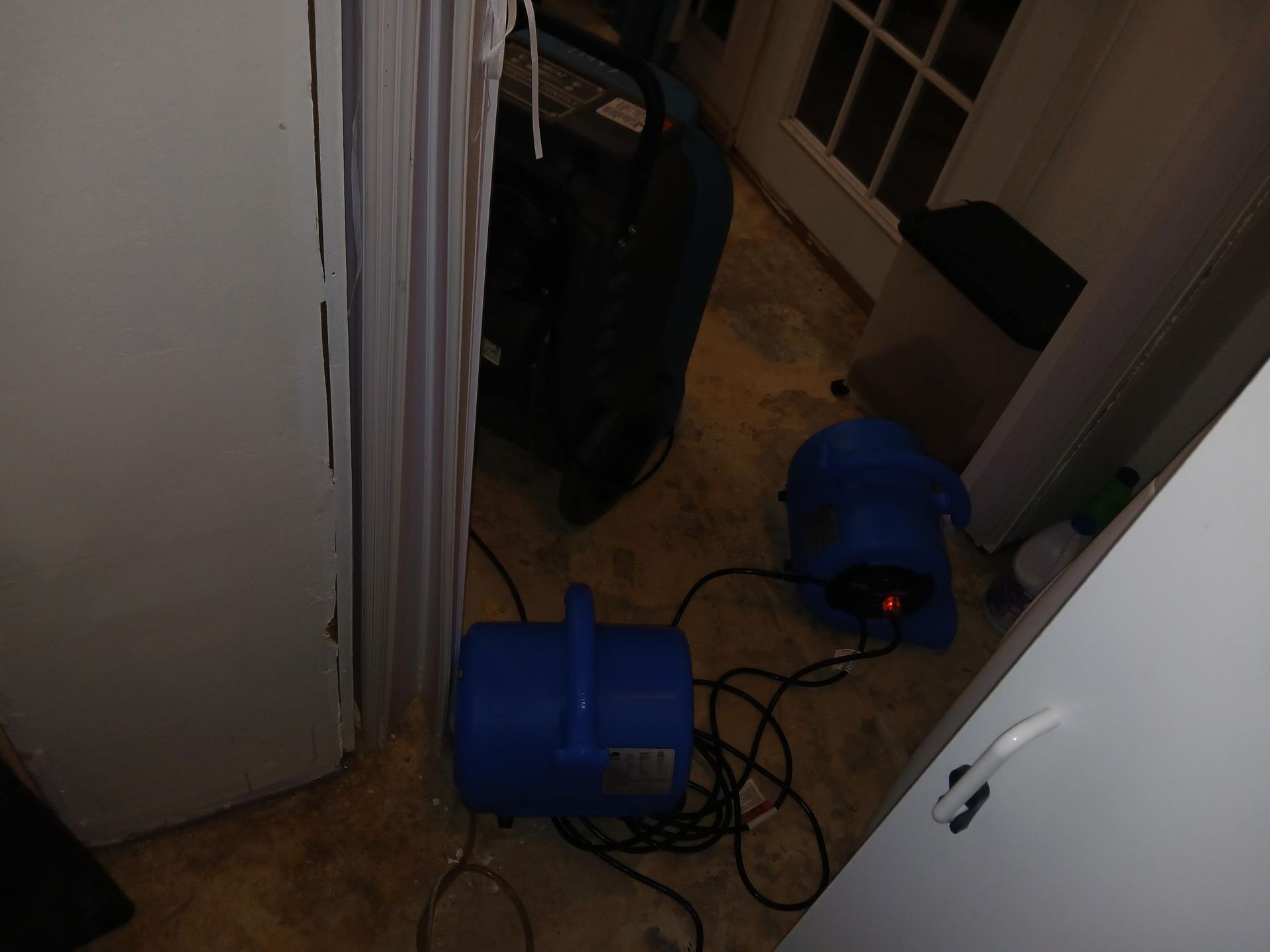 Two blue fans and a black dehumidifier in a room with a closed white door.