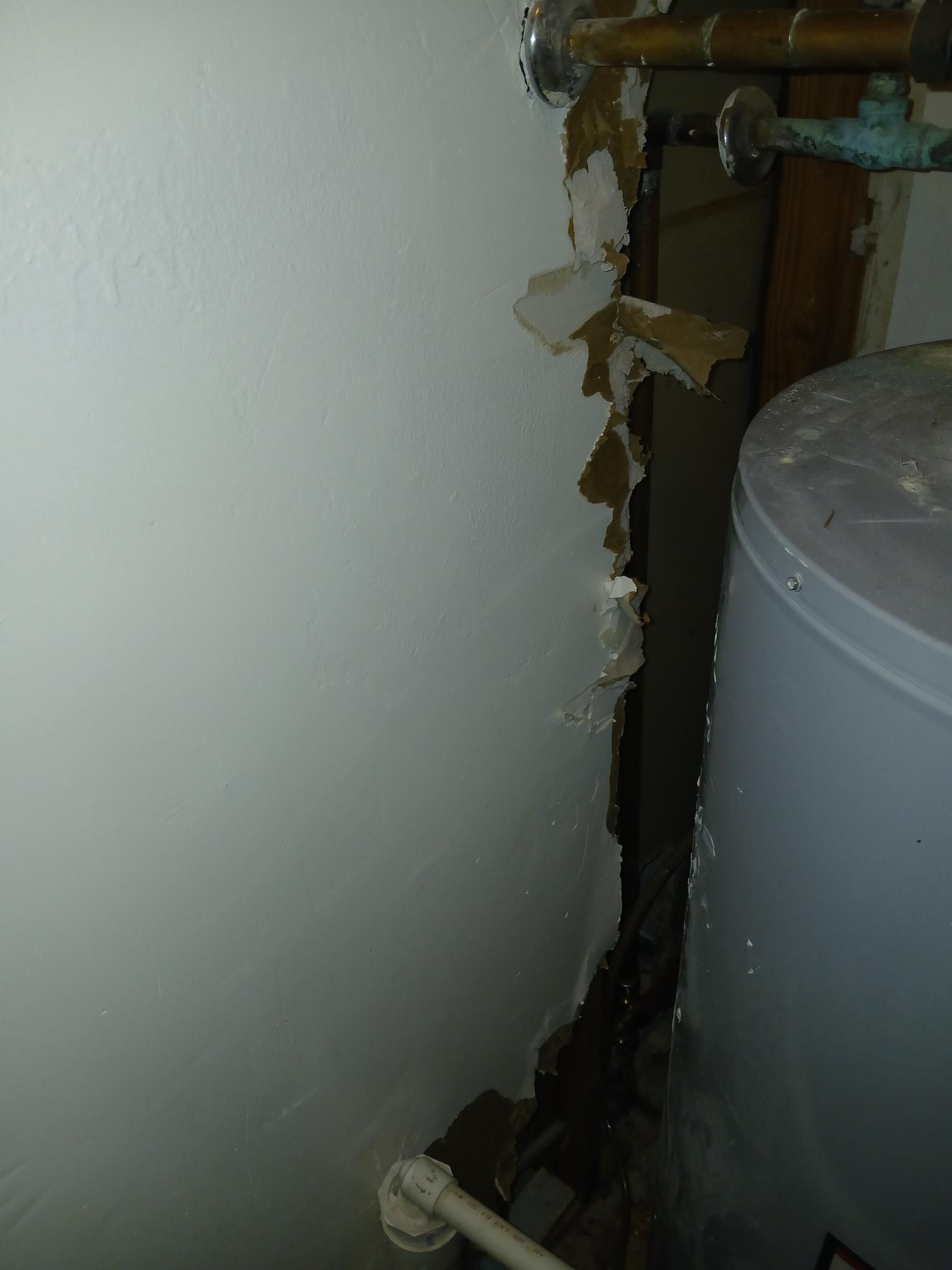Damaged wall next to a water heater, with peeling paint and exposed materials.