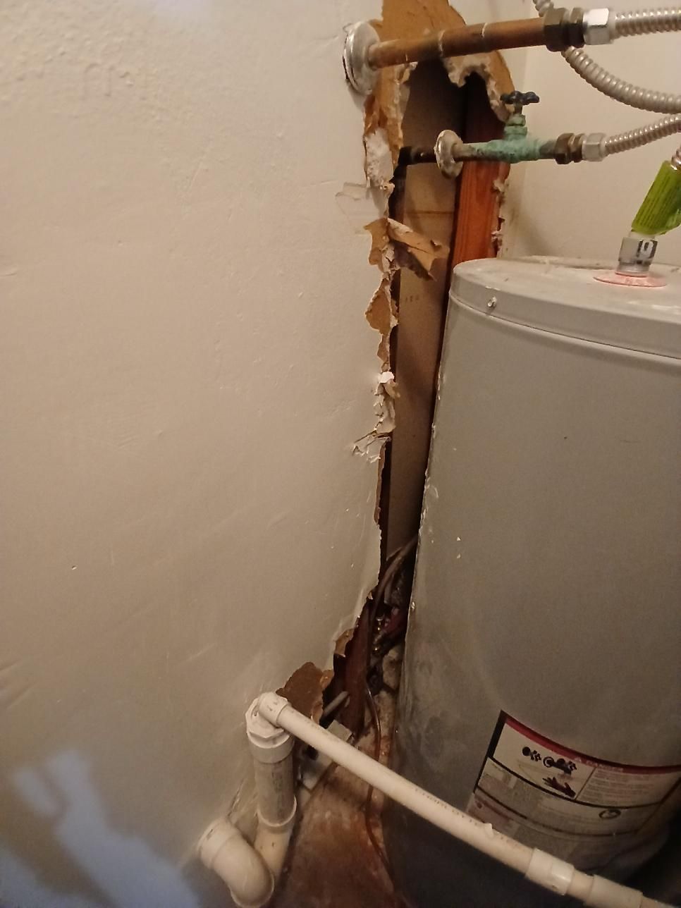 Damaged wall next to a water heater; exposed framing and pipes, with signs of water damage.