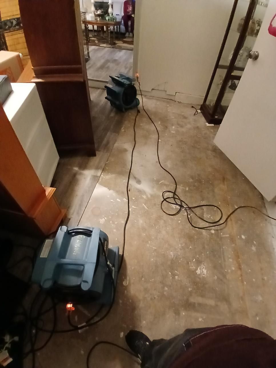 Two blue air movers on concrete floor, electrical cords, doorway, and furniture in room.