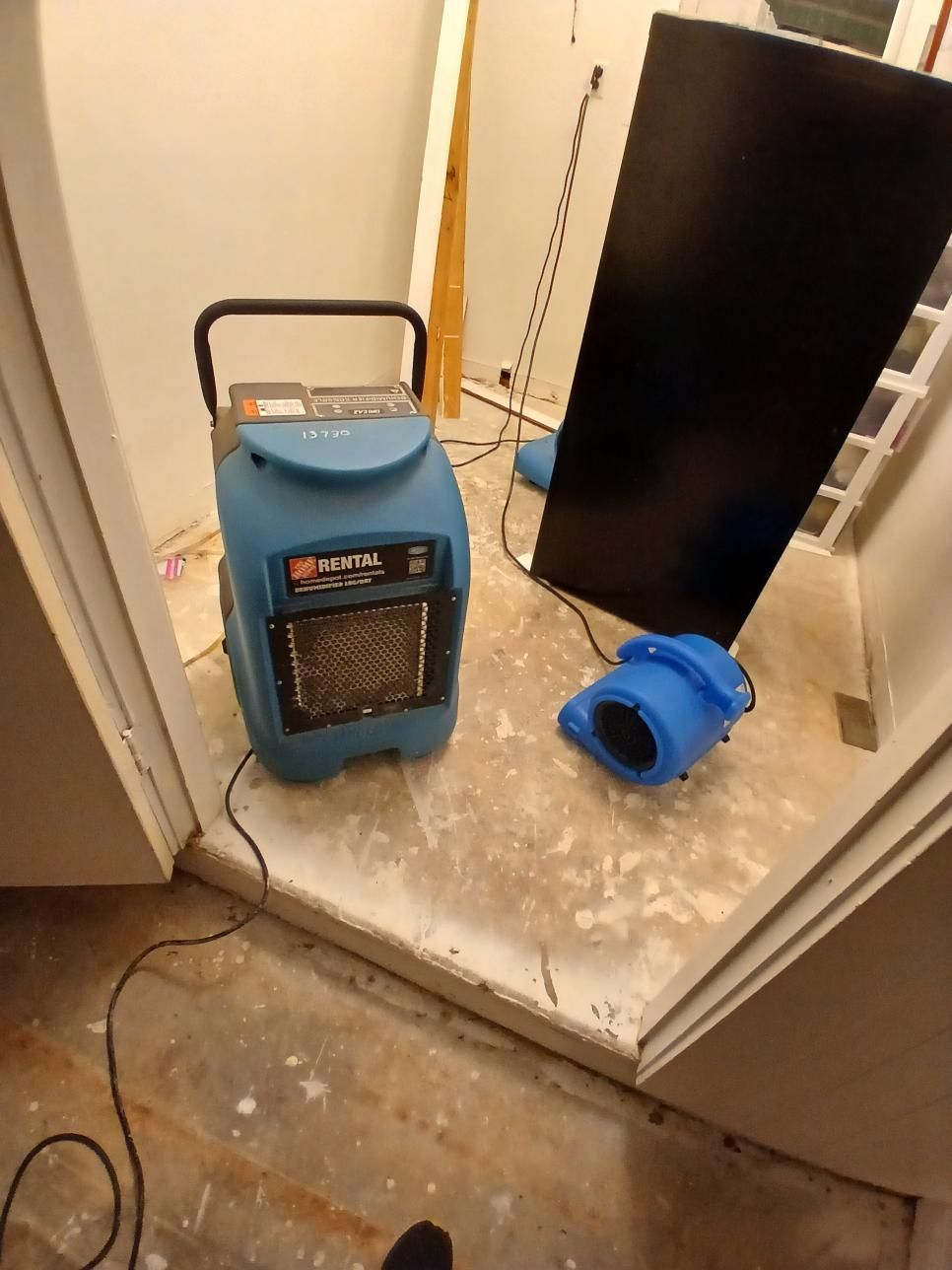 Blue dehumidifier and blower inside a room with damaged flooring.
