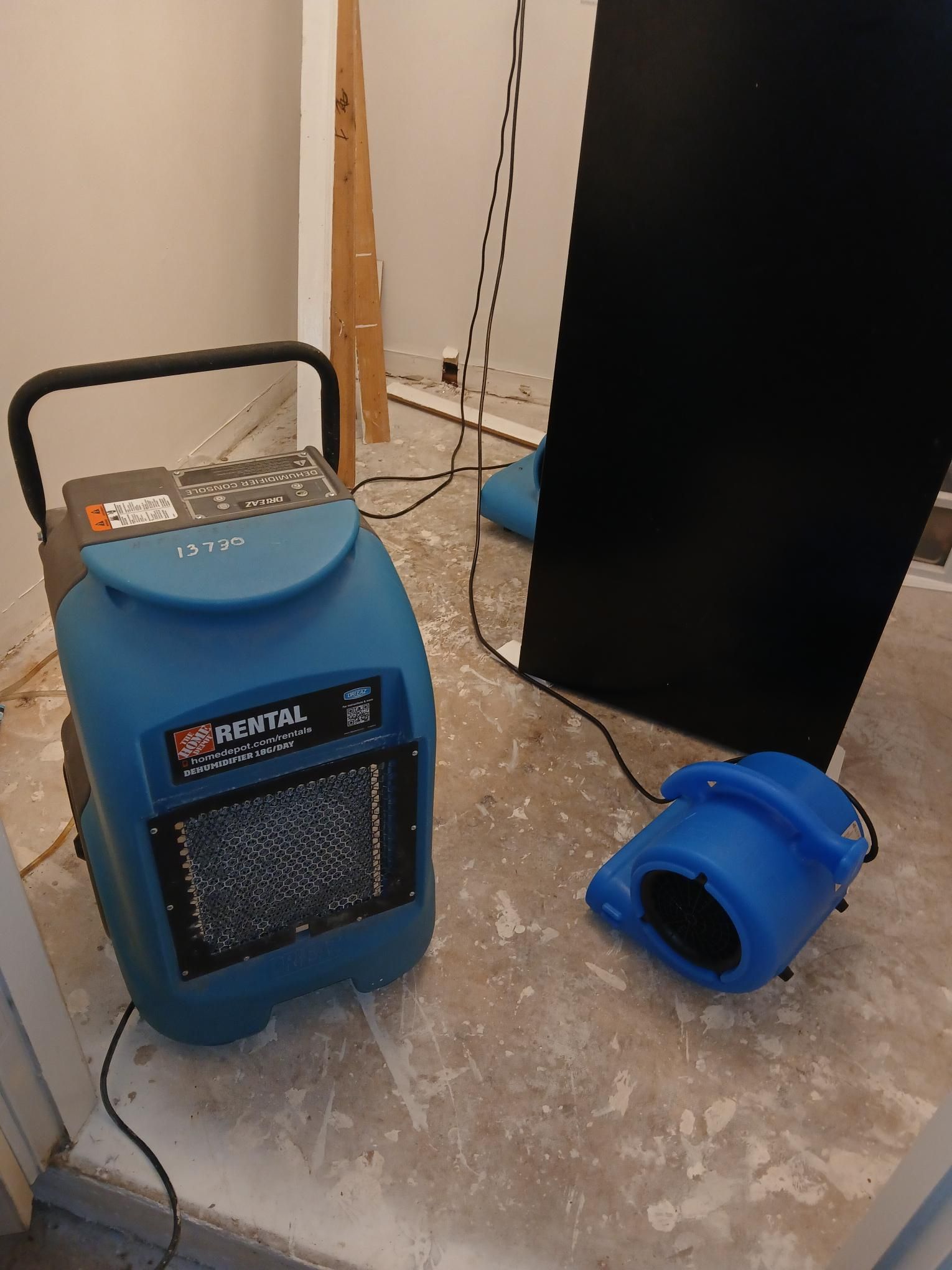 Blue dehumidifier and fan on a concrete floor in a room under construction.