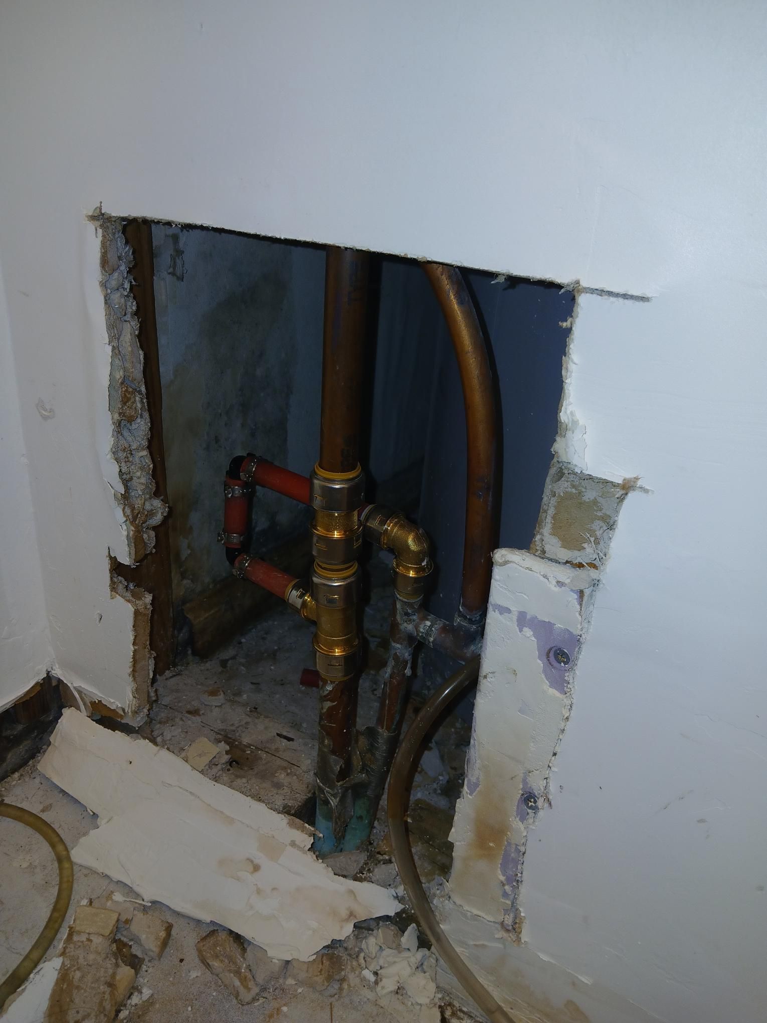 Copper pipes exposed through a hole in a wall, likely plumbing repair.