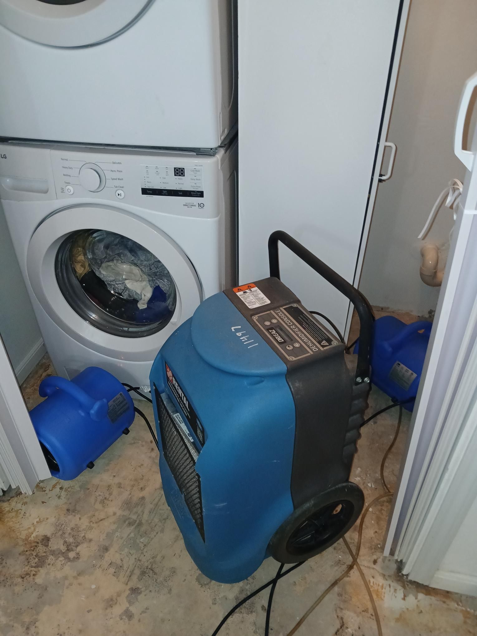 Dehumidifier, blower fans, and washer/dryer in a laundry area, likely for moisture remediation.