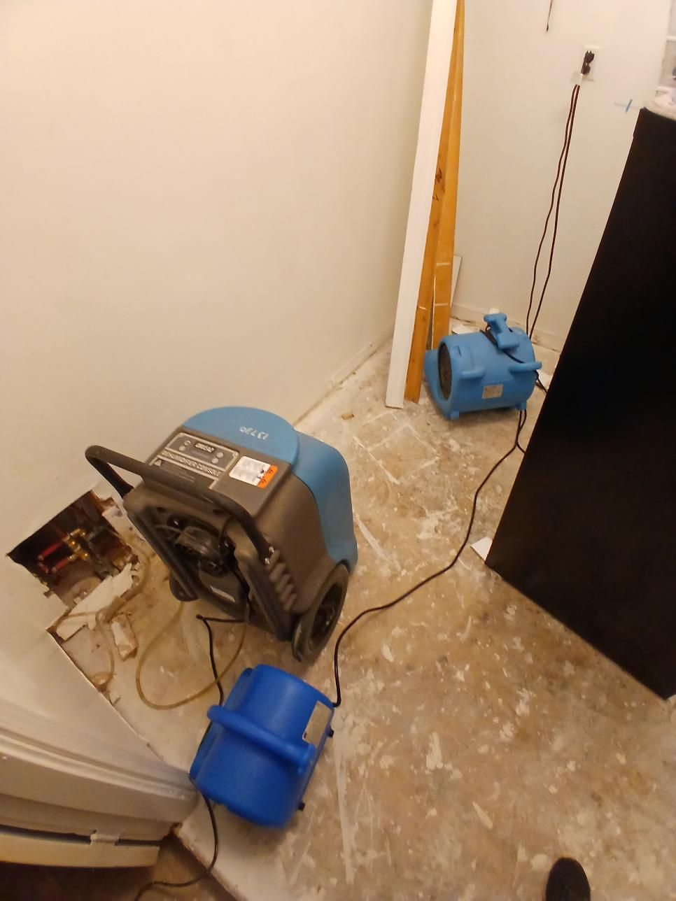 Two dehumidifiers and a blower fan in a room with exposed flooring.