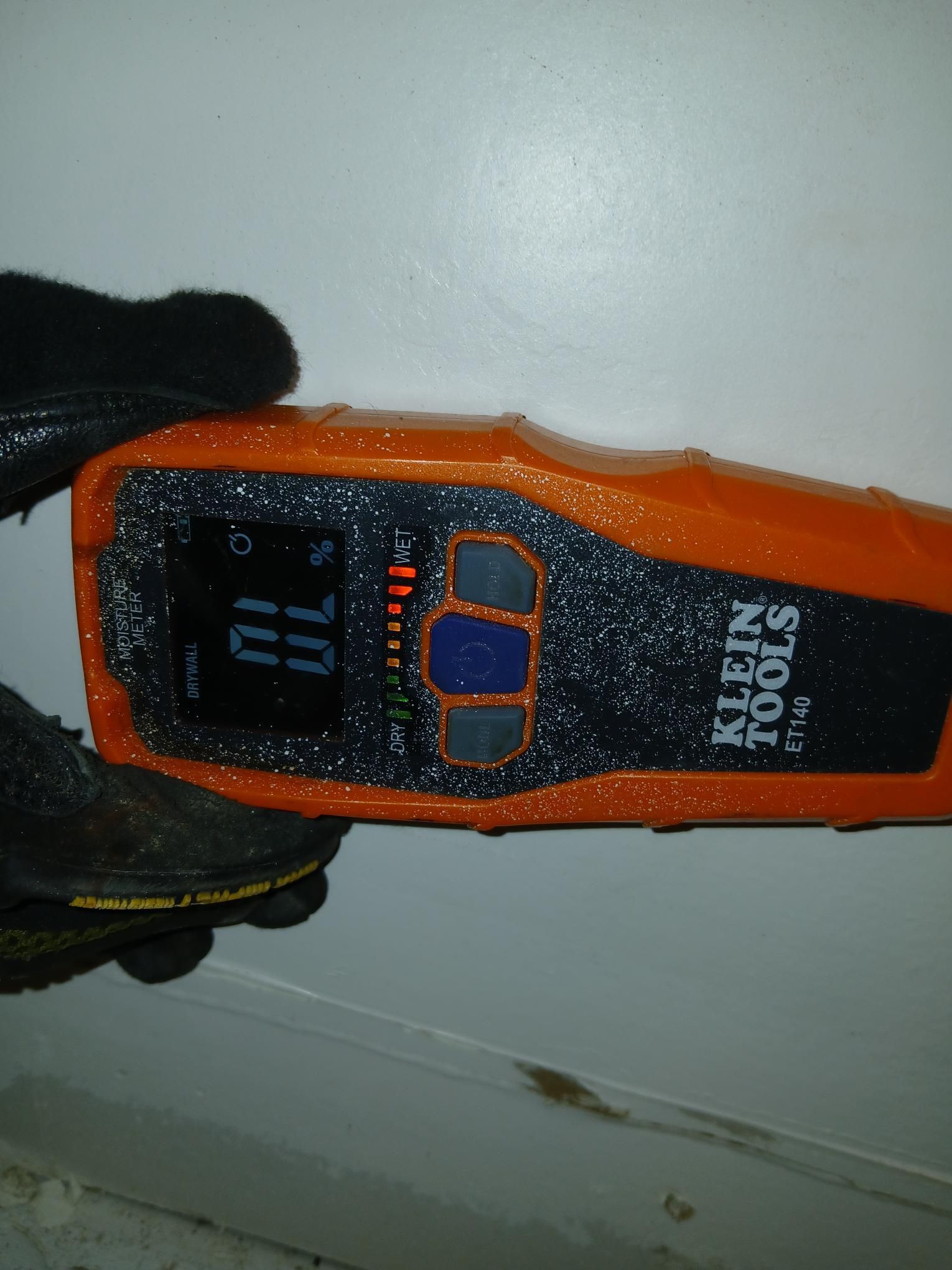 A person holding an orange Klein Tools ET40 stud finder against a white wall; the display reads 