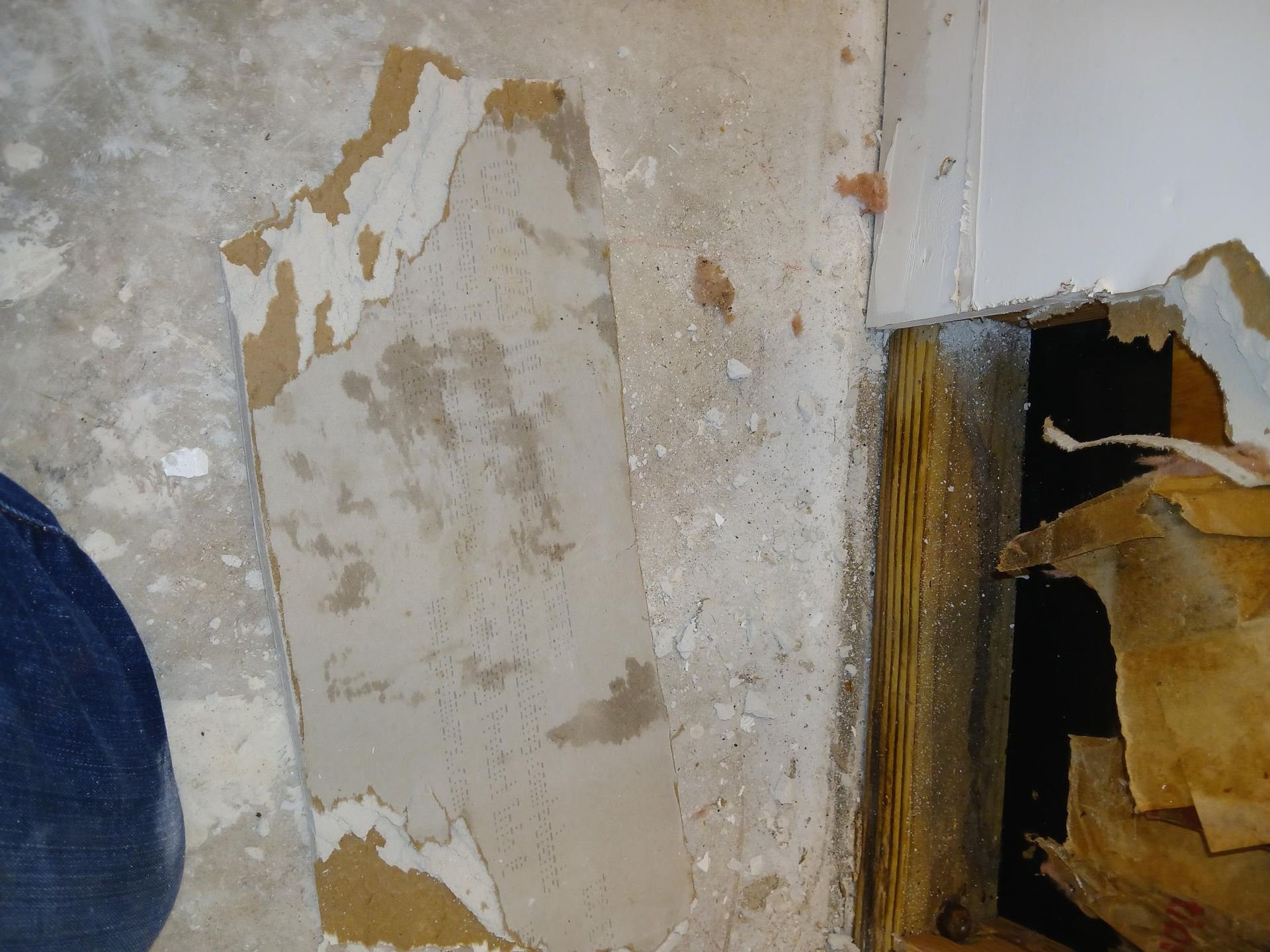 Damaged wall with peeling paint and exposed wood framing.