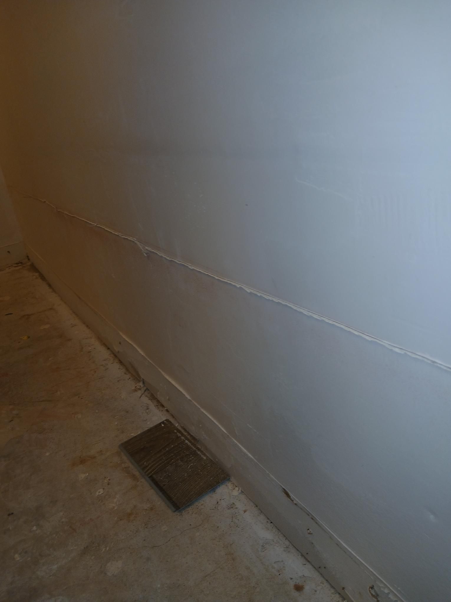 Gray wall with a diagonal crack and a floor vent in a corner.