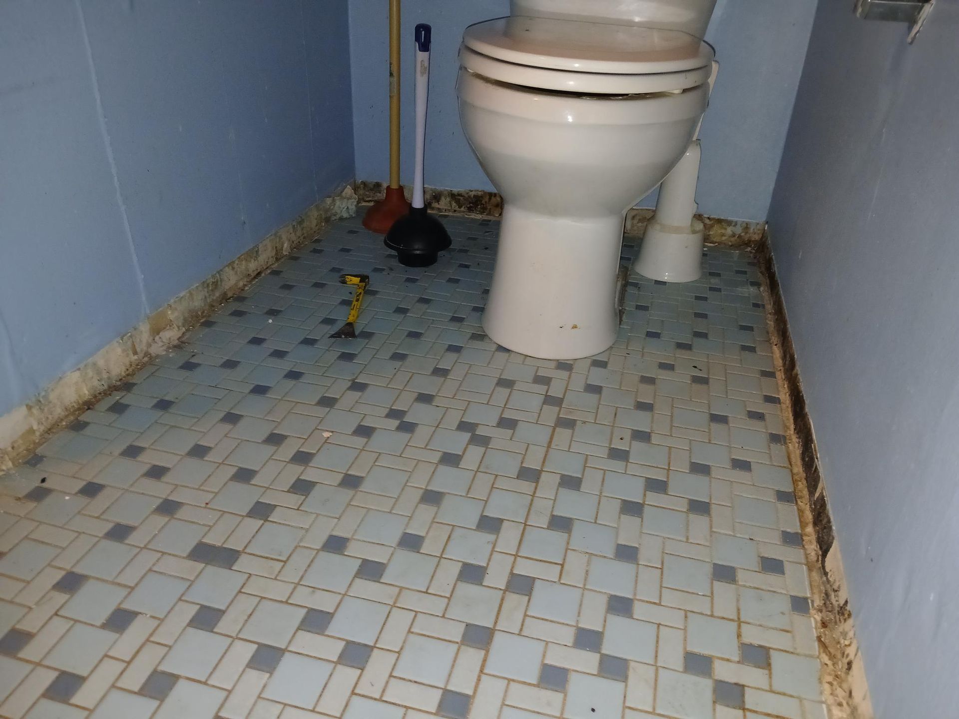 Bathroom with blue and gray tile floor, white toilet, and cleaning tools.