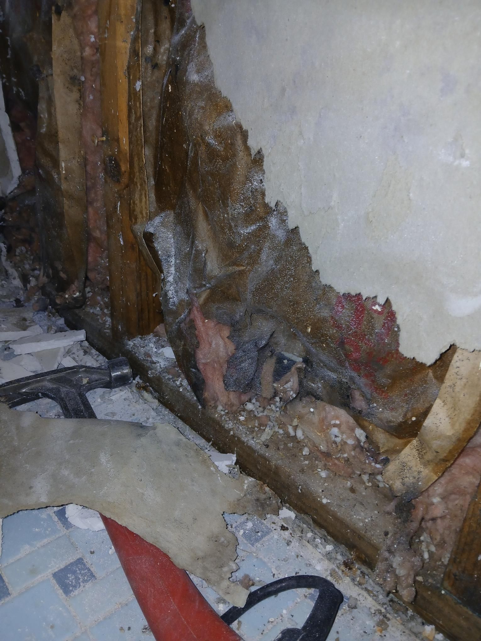 Damaged wall with exposed wood, insulation, and debris. Brown wood framing, white and pink insulation, light wall.