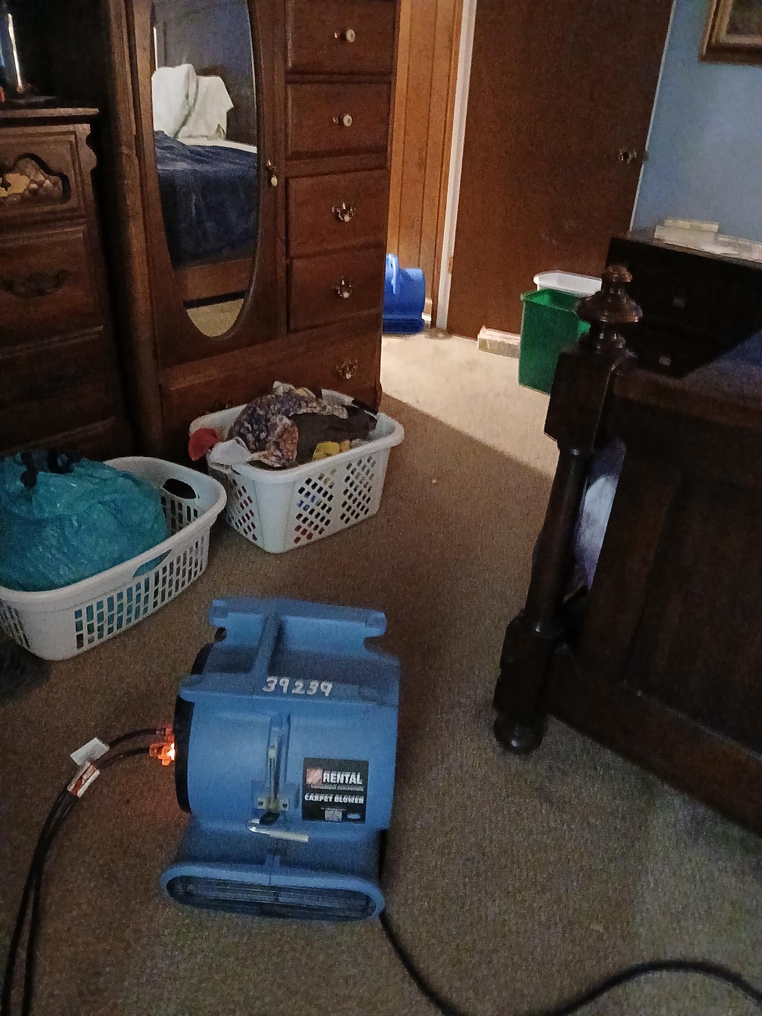 Blue air mover on carpeted floor; bedroom with furniture and laundry baskets.
