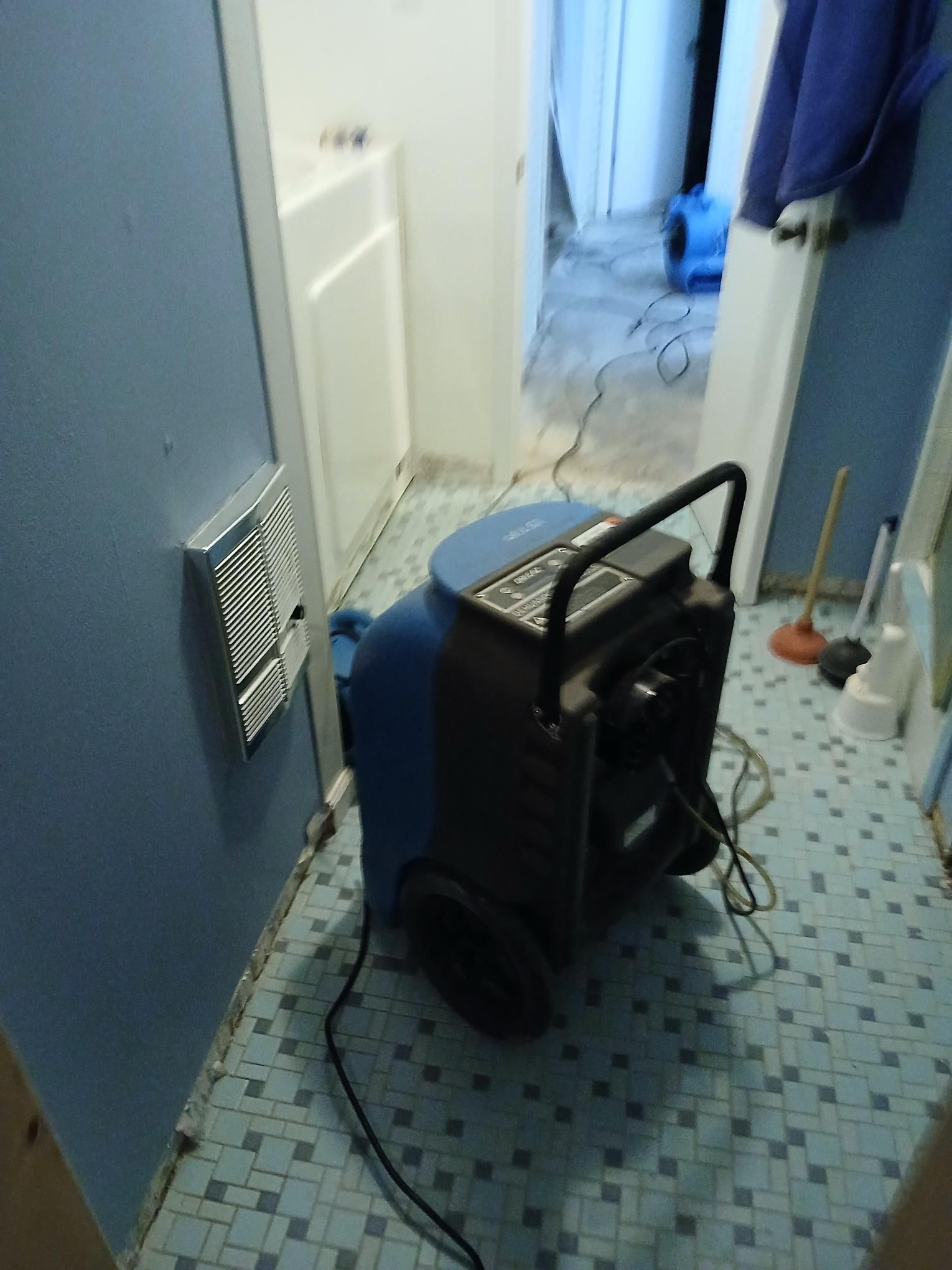 Blue and black dehumidifier in a bathroom with blue tile flooring.