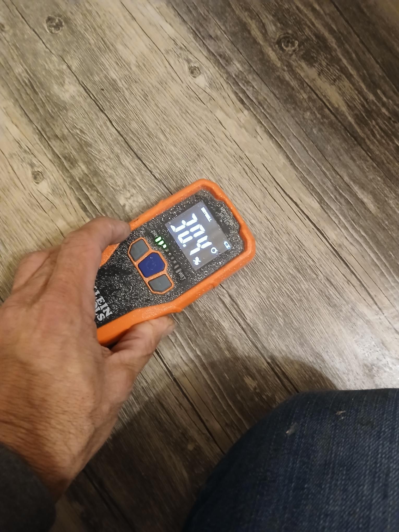 Person holding an orange device over wood flooring; device reads 30.4°.
