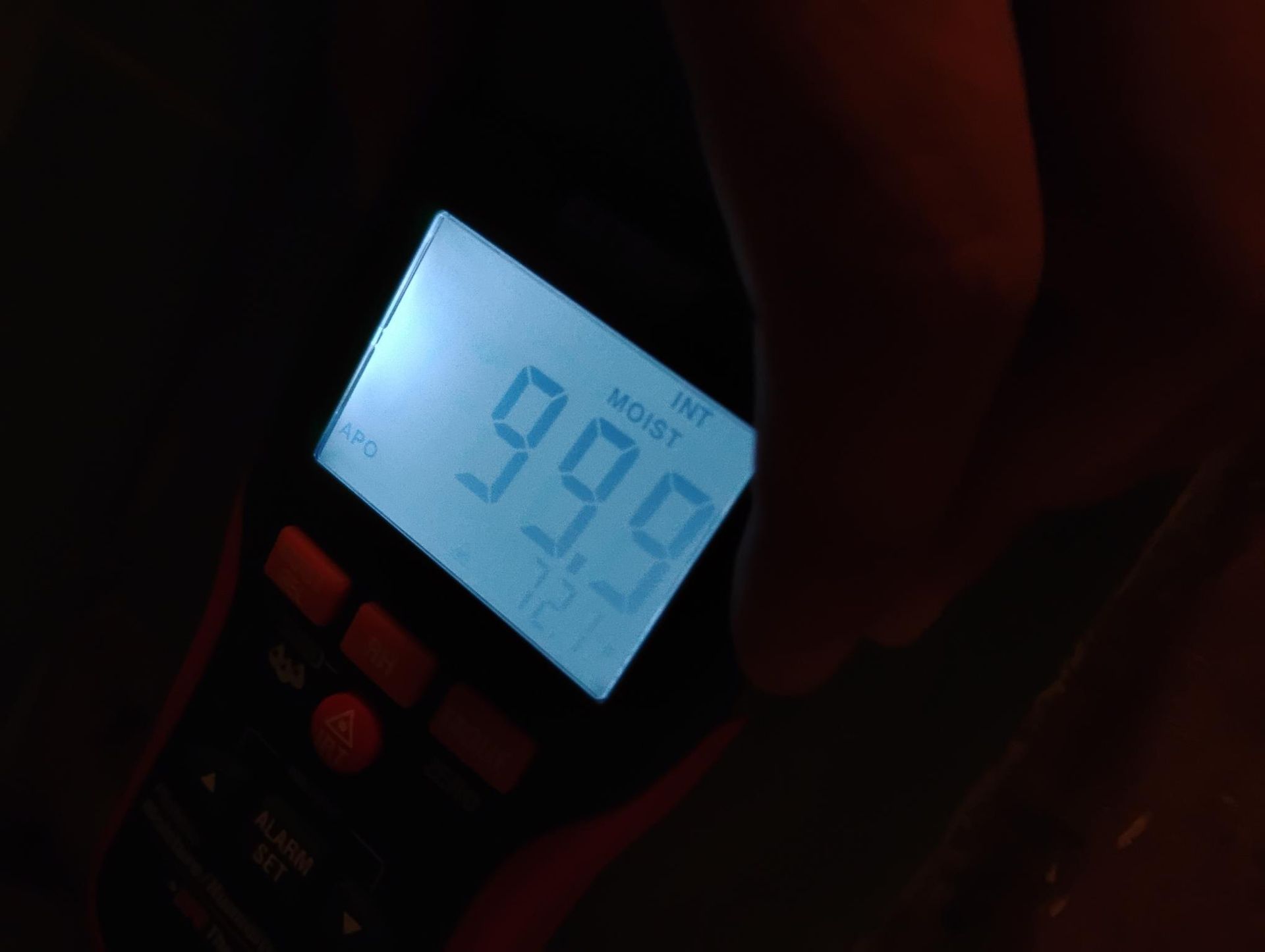 A hand holding a moisture meter; display reads 99.9, with the words 