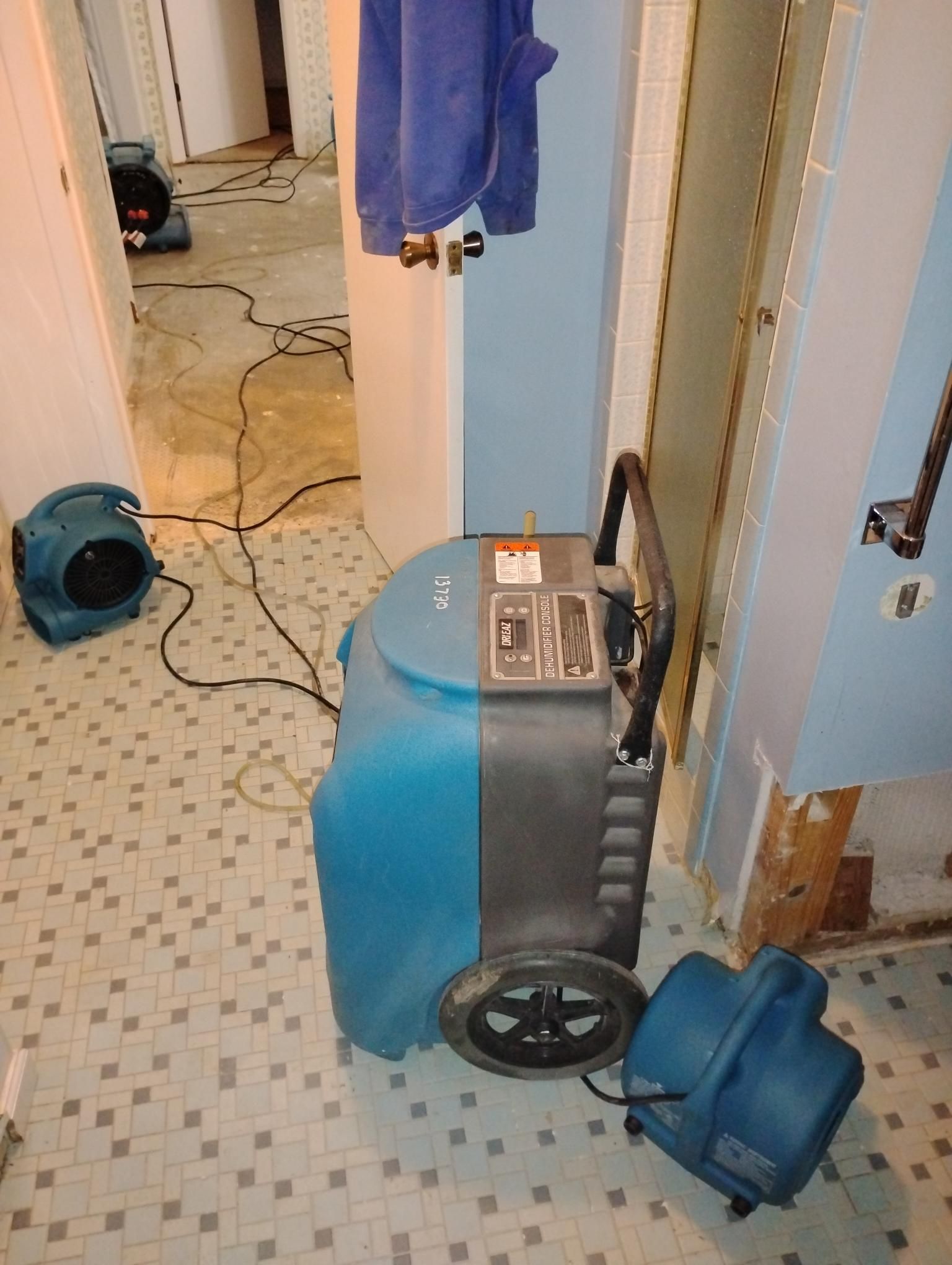 Blue dehumidifier and fans in a tiled bathroom, likely drying after water damage.