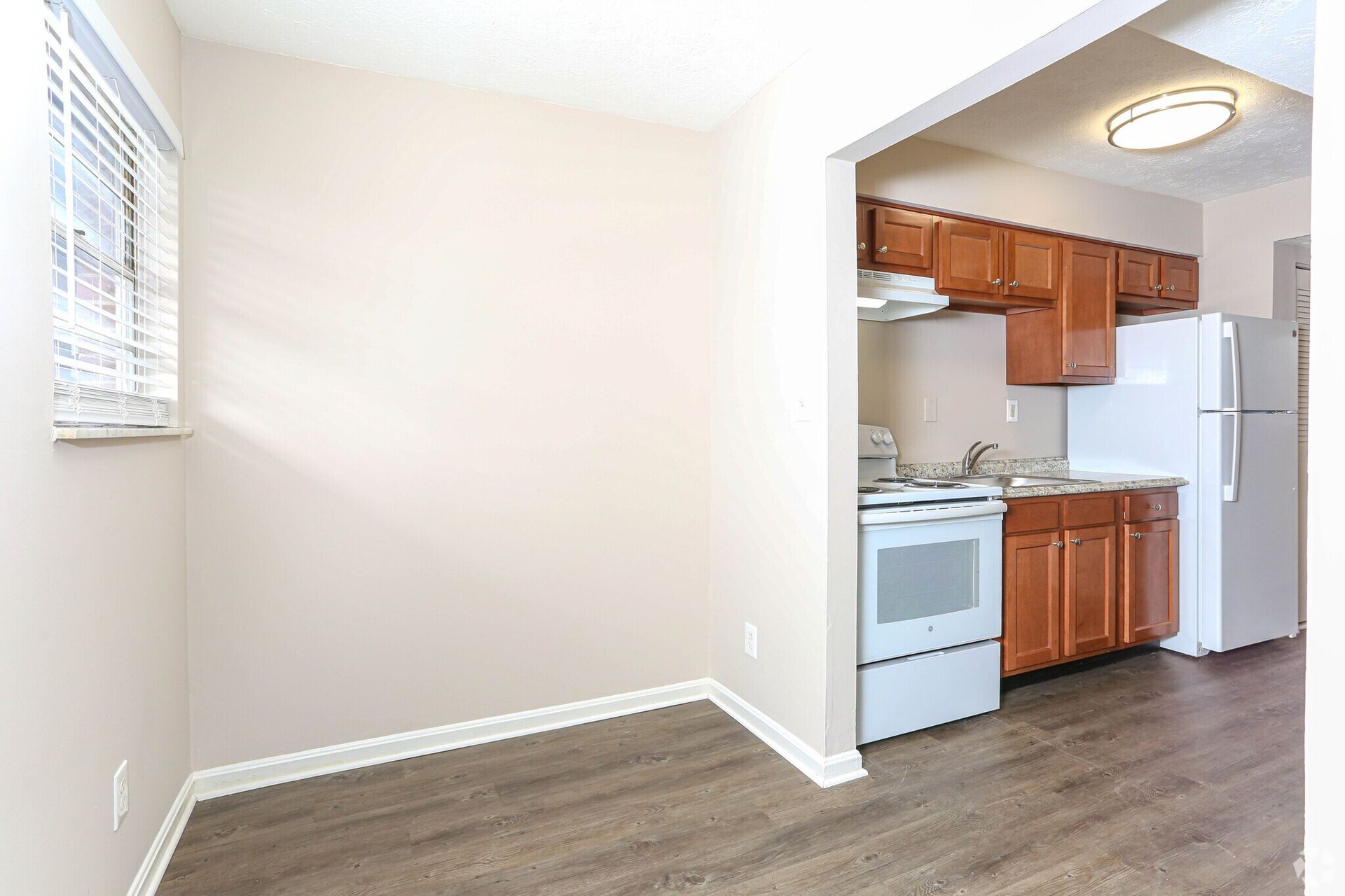 A kitchen with wooden cabinets , a white refrigerator , a stove , and a window.