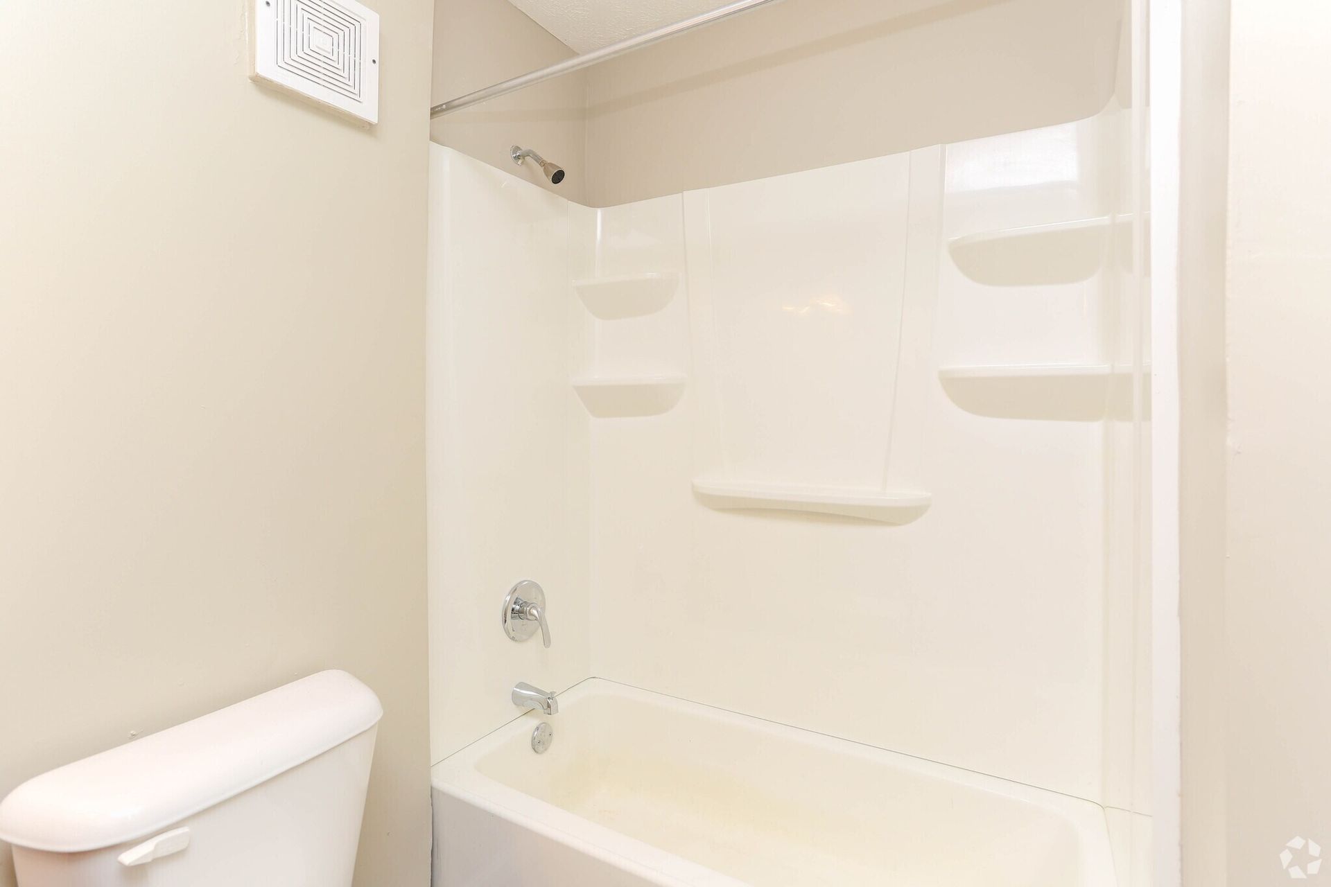 A bathroom with a toilet , bathtub , shower and shelves.