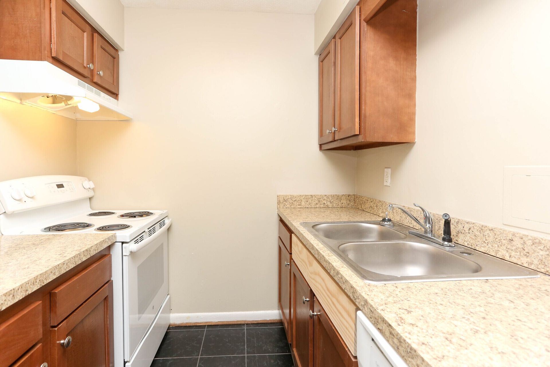 An empty kitchen with a stove , sink , and dishwasher.