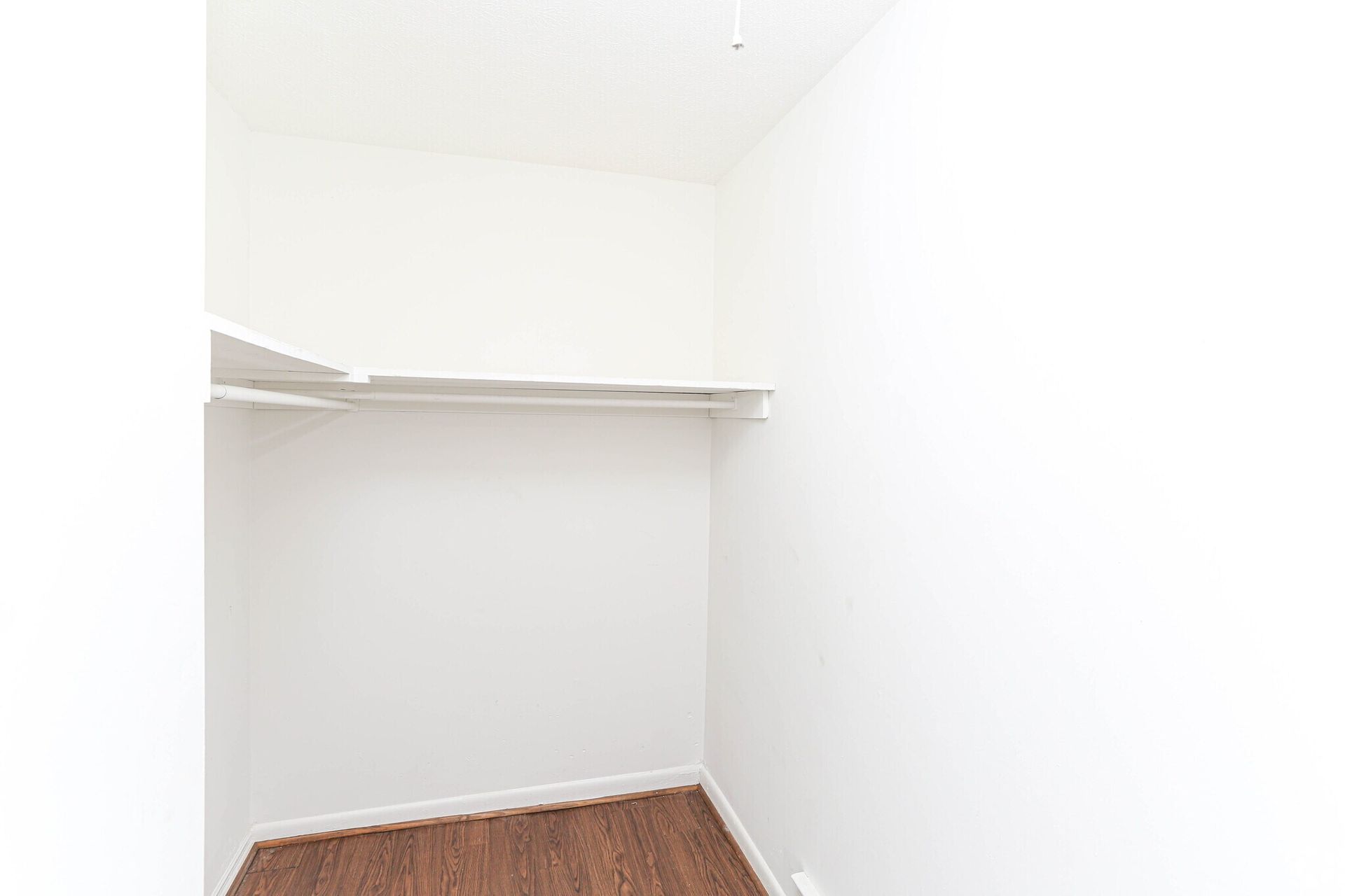 An empty walk in closet with hardwood floors and white walls.