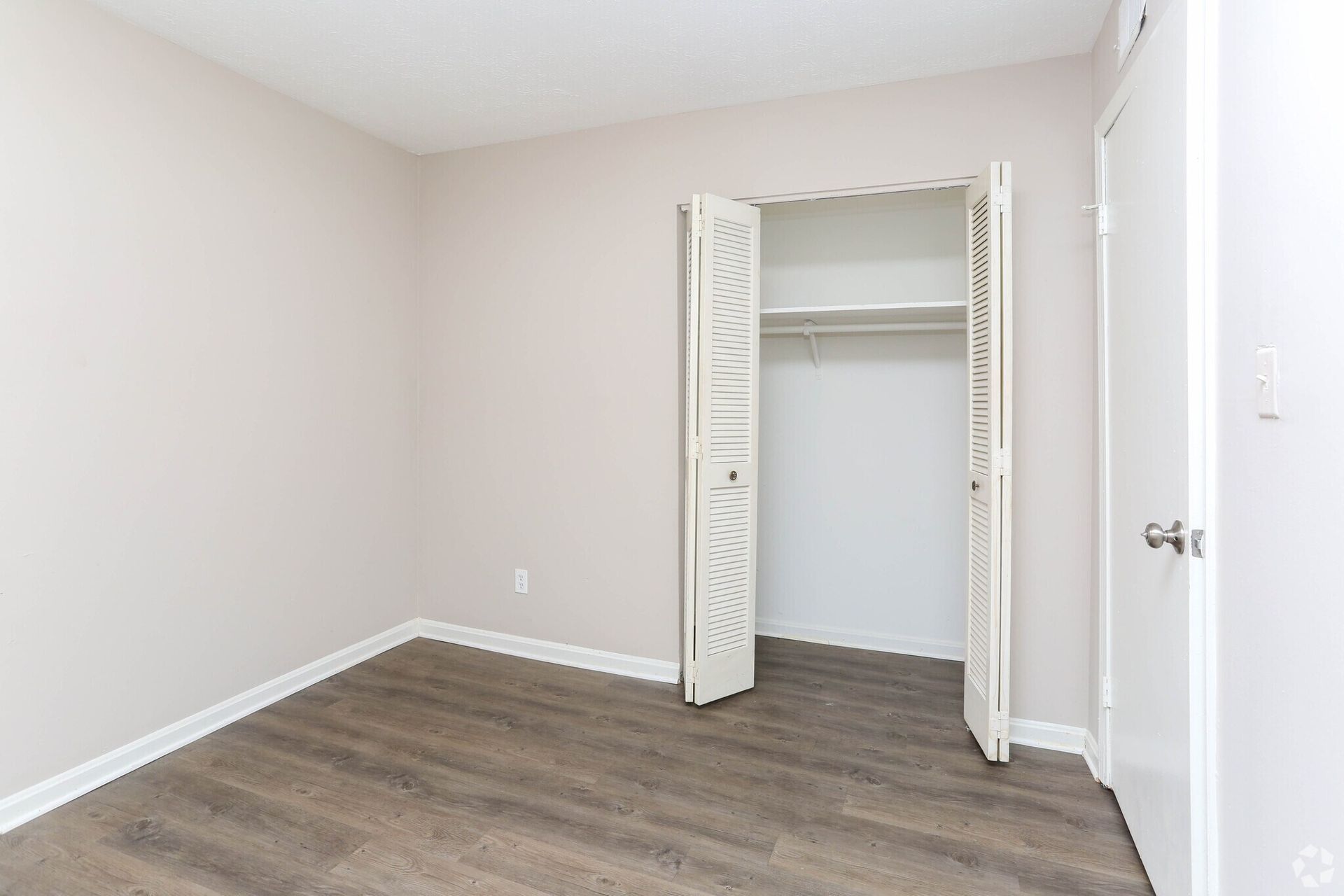 An empty bedroom with hardwood floors and a closet.