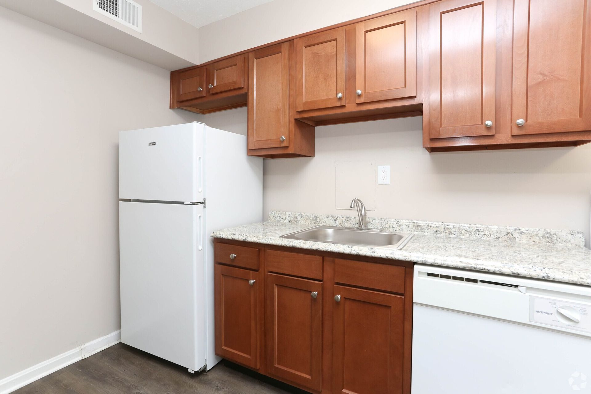 A kitchen with wooden cabinets , a white refrigerator , a sink , and a dishwasher.