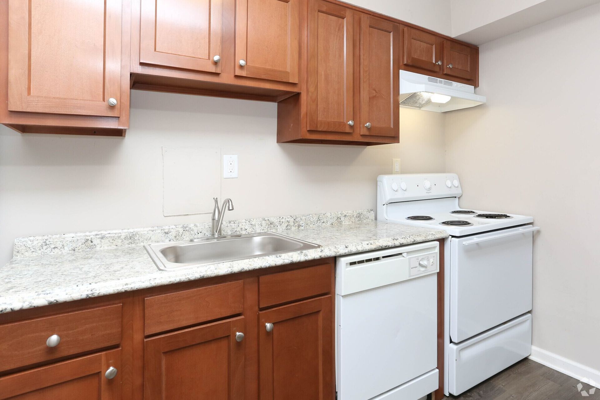 A kitchen with wooden cabinets , a white stove , a sink , and a dishwasher.