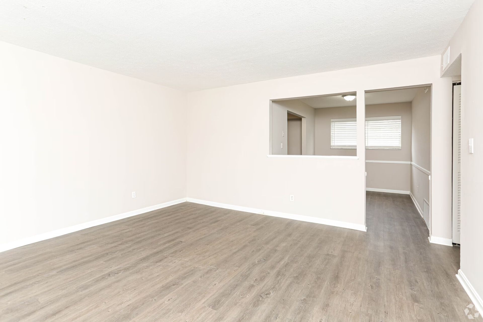 An empty living room with hardwood floors and white walls.