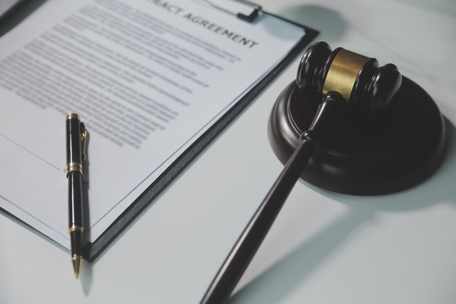 Contract agreement document on a clipboard with a gavel and pen on a white surface.
