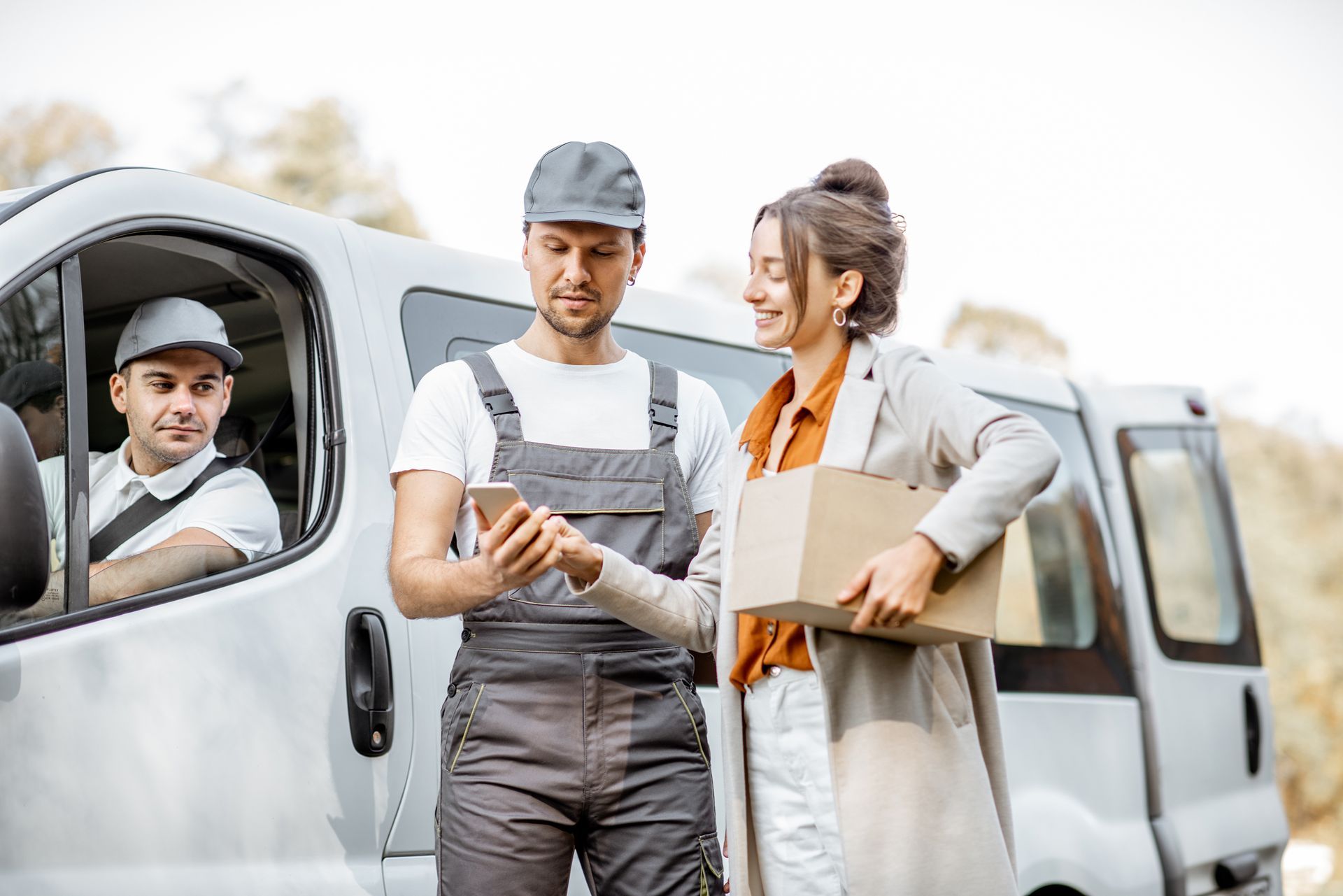 A delivery man is giving a package to a woman in front of a van.