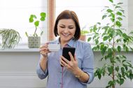 A woman is holding a cup of coffee and looking at her cell phone.