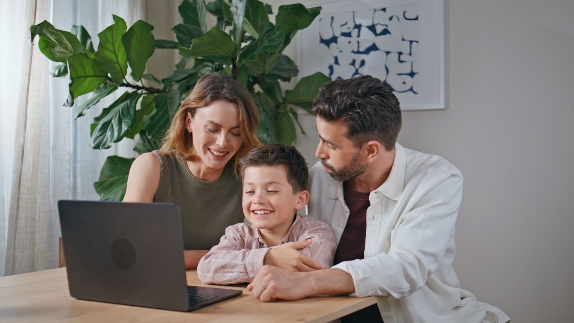 A family is sitting at a table looking at a laptop computer.