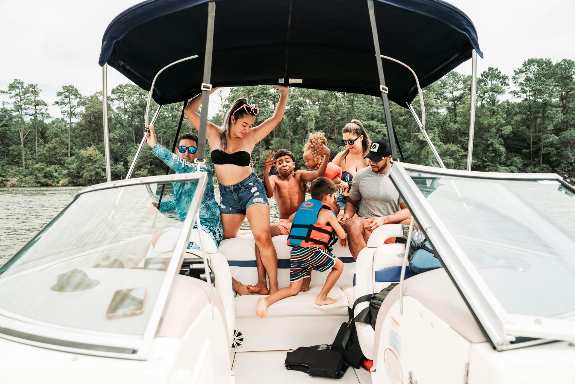 Group of people on a boat, smiling and posing near a body of water, forest in the background.