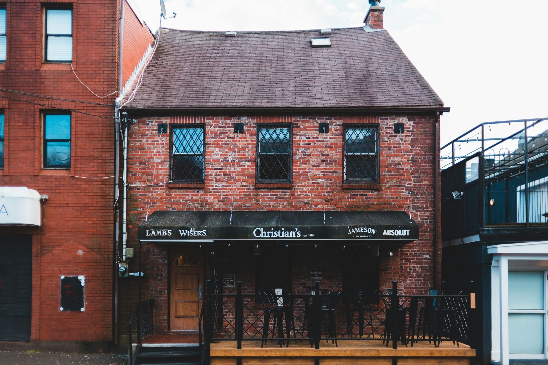 Red brick building with a Christian's bar and awning. The building has three windows, and a small wooden patio with a black fence.