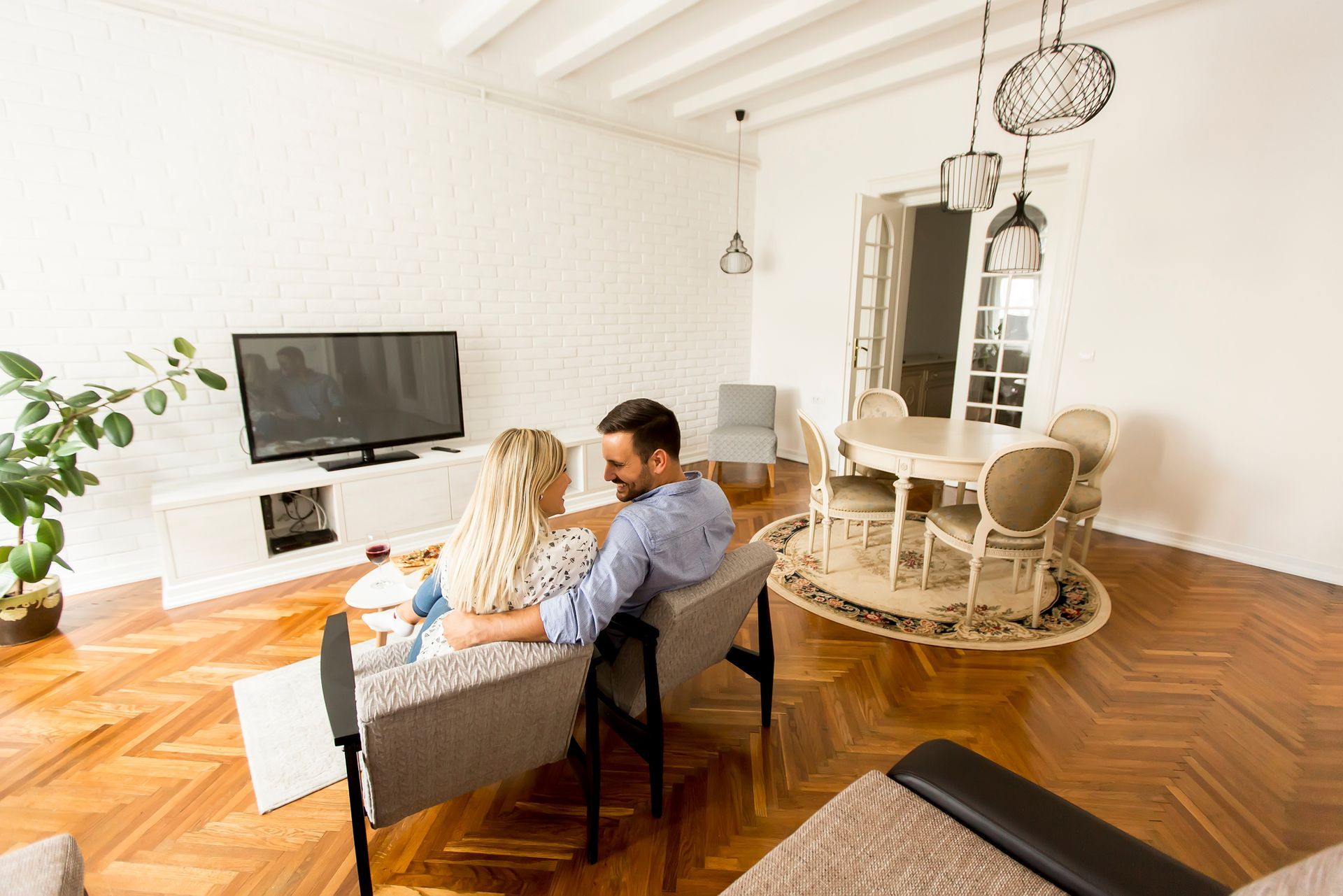 A man and a woman are sitting on a couch in a living room watching tv.