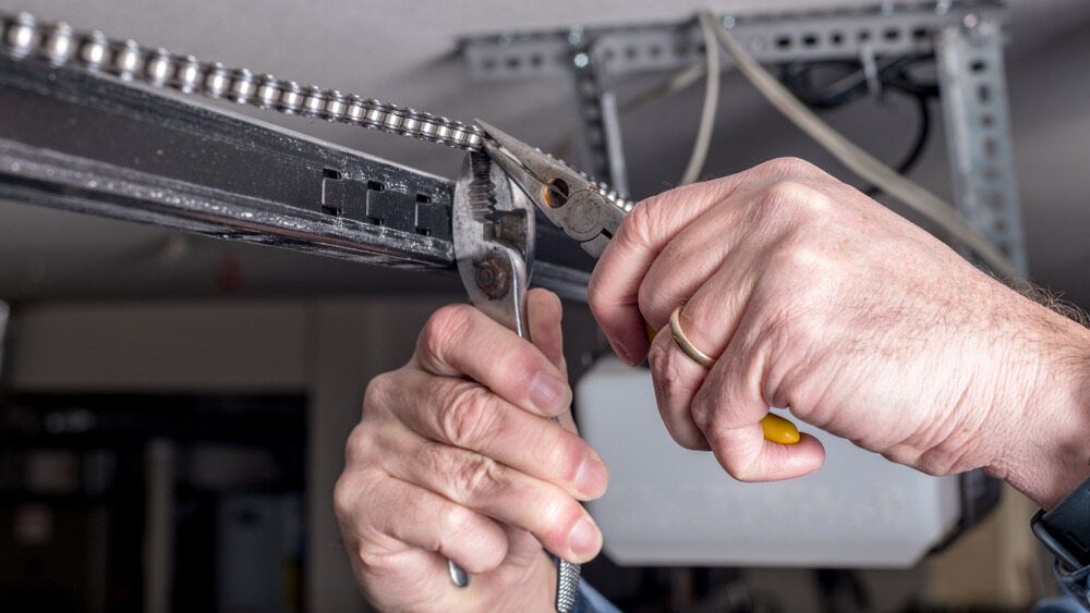 Person Using Pliers and Wrench to Work on a Garage Door Opener Chain in a Garage — Duncan's Doors In Kearneys Spring, QLD