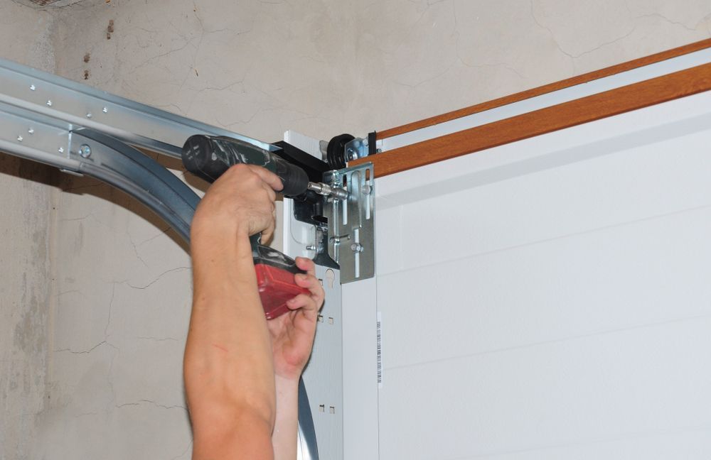 Person Using a Power Drill to Install a Component on a White Garage Door Track — Duncan's Doors In Kearneys Spring, QLD