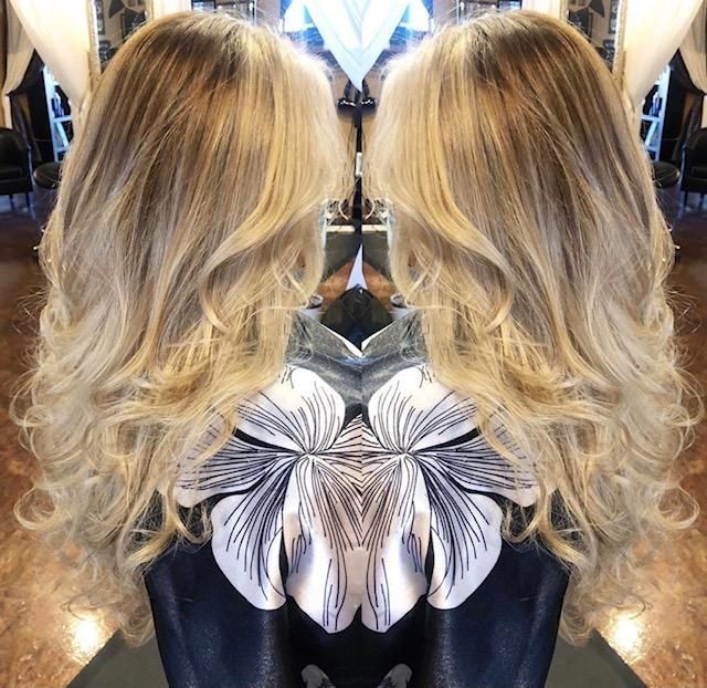 Mirrored view of long wavy blonde hair with dark roots and a black-and-white floral top