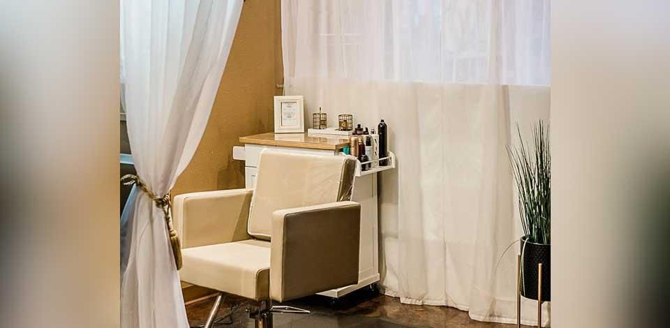 Beige salon chair in a softly lit spa room with white curtains and shelves of beauty products