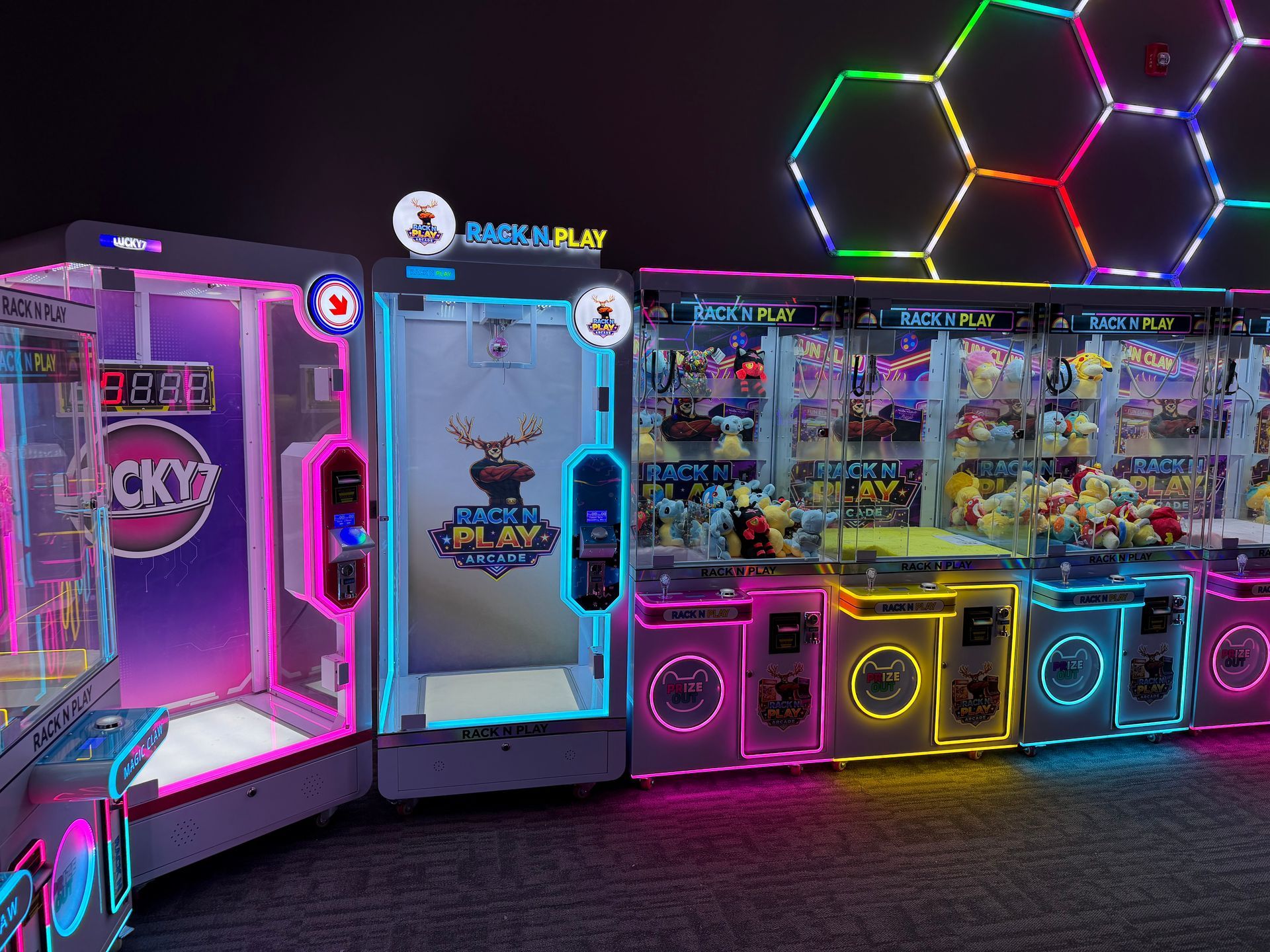 Neon-lit arcade prize machines with colorful glowing outlines and a honeycomb light display above.