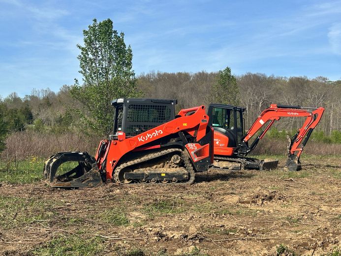 A bulldozer and an excavator are sitting in a field.