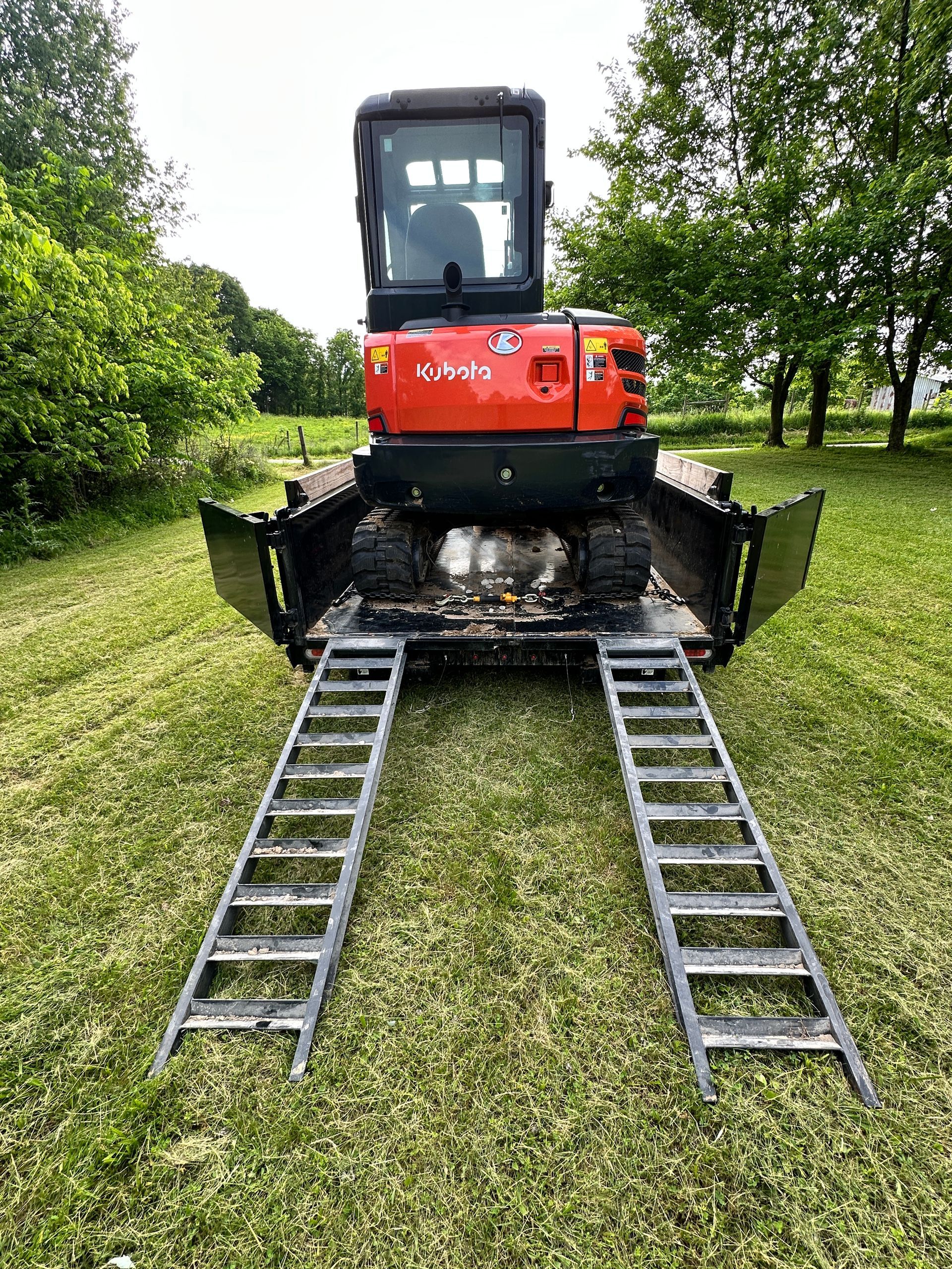A red excavator is parked on a trailer with ladder ramps.