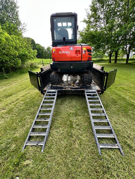 A red excavator is parked on a trailer with ladder ramps.