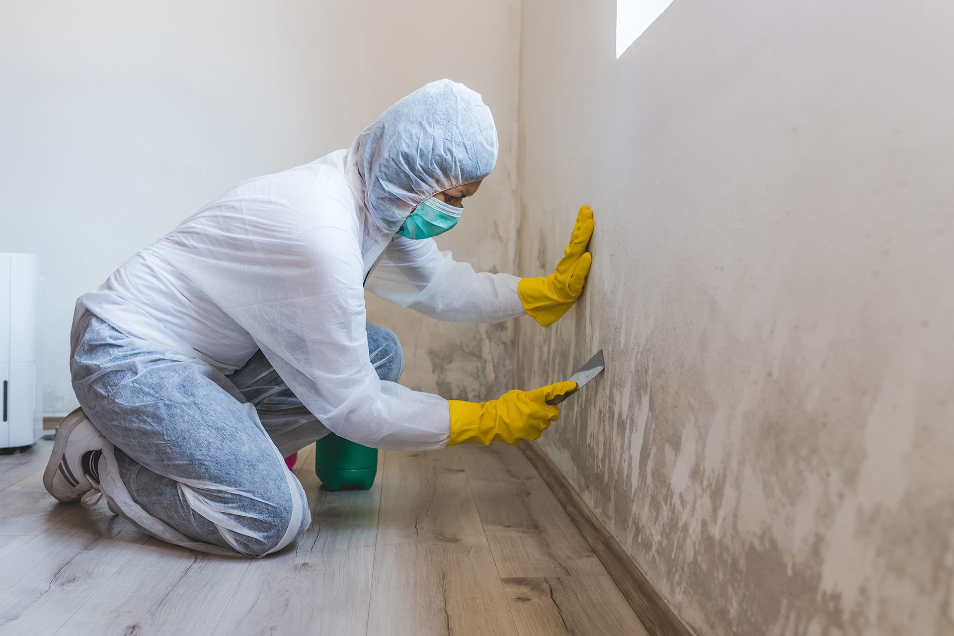 A man in a protective suit and mask is cleaning a wall.